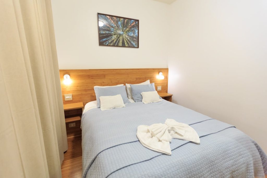 blue-bed-linen-on-bed-13871310 Inviting hotel room featuring elegant blue bedding, wooden headboard, and ambient lighting for a warm ambiance.