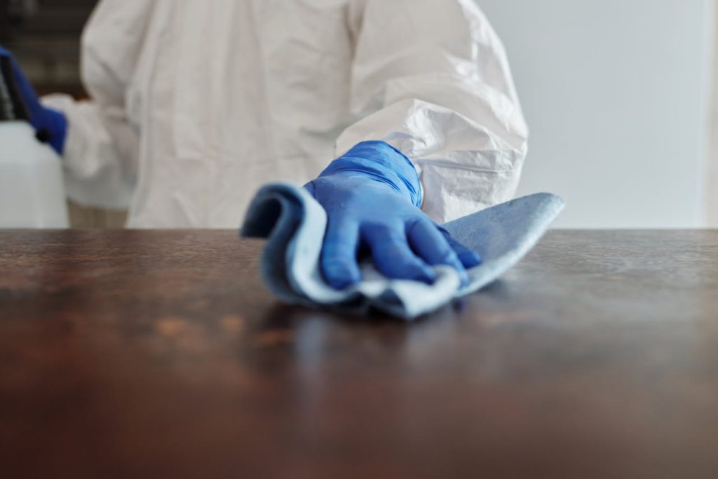 close-up-photo-of-person-cleaning-the-table-4099467 Person in protective suit using disinfectant on surface to ensure cleanliness and safety.