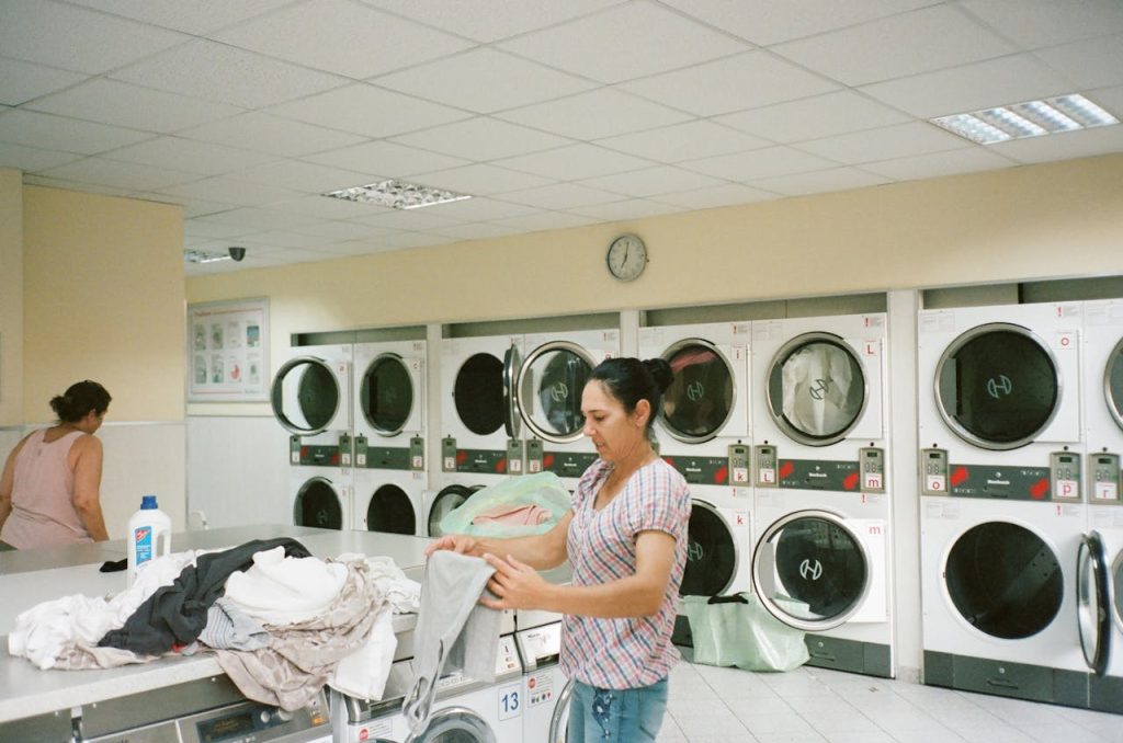 photo-of-woman-standing-inside-the-laundromat-2927523 A woman folding clothes in a modern laundromat with various washing machines in the background.