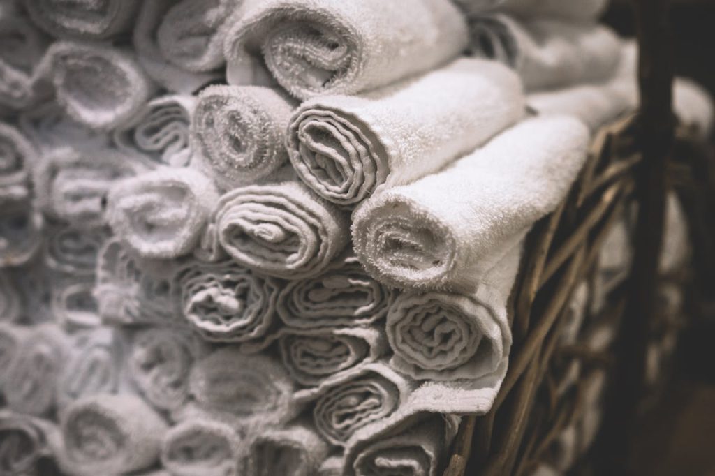 white-textile-lot-282892 Stack of neatly rolled white towels in a woven basket, perfect for spa or bathroom settings.